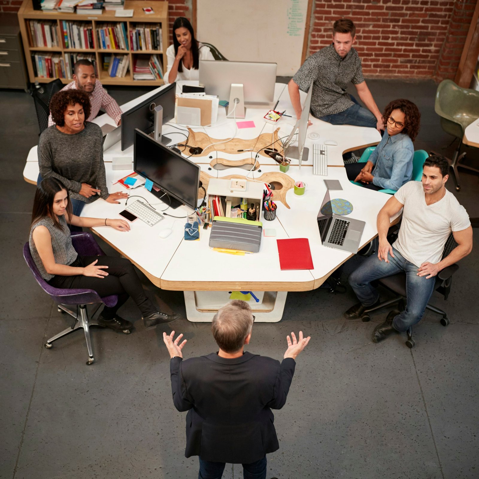 Senior Businessman Talking At Meeting Of Casually Dressed Business Team In Open Plan Office