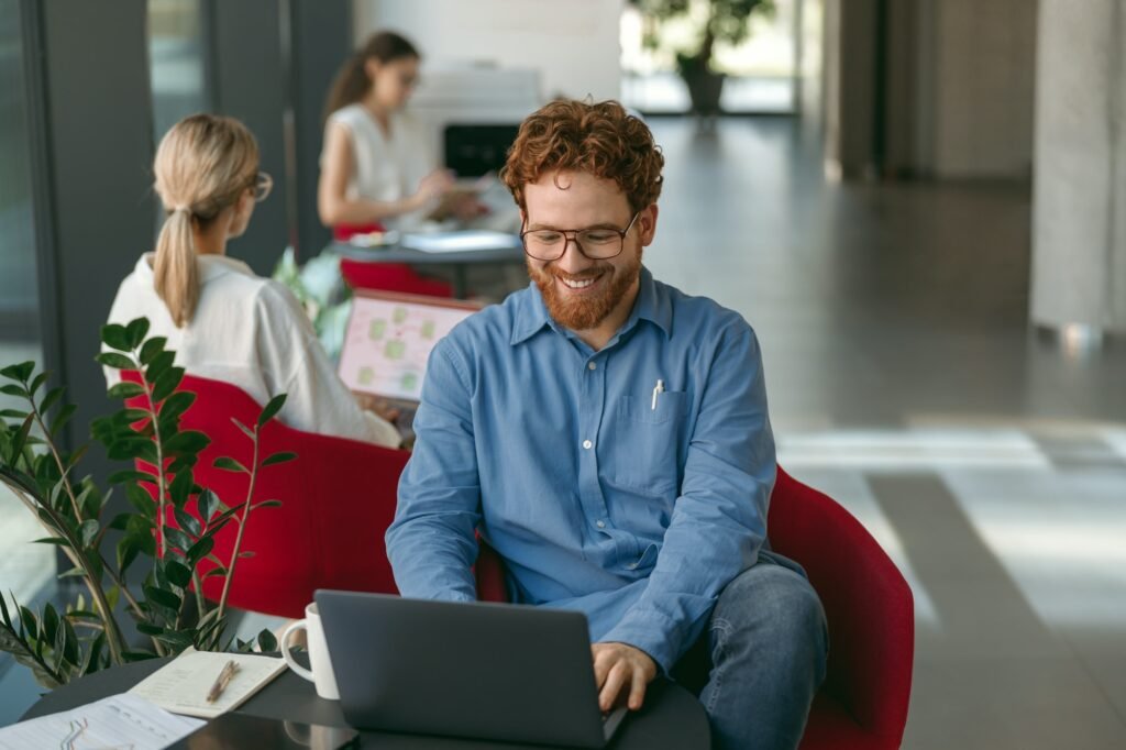 Smiling male sales manager in eyeglasses working on laptop sitting in office during working day